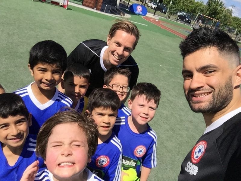 Dani en Melbourne estudiante Dani con su equipo de niños pequeños de fútbol y otro entrenador sonriendo y con el uniforme azul
